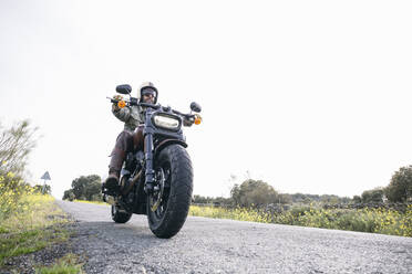 Männlicher Motorradfahrer mit Helm auf der Straße gegen den klaren Himmel - ABZF03151