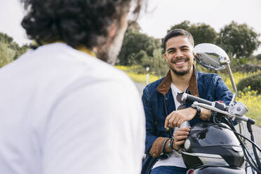 Smiling man talking with biker while sitting on motorcycle - ABZF03153