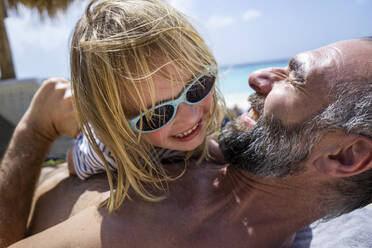 Nahaufnahme eines fröhlichen Mädchens mit Sonnenbrille, das mit seinem Vater ohne Hemd am Strand spielt - JLOF00419