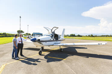 Pilot und Co-Pilot sitzen auf der Startbahn und unterhalten sich vor einem Sportflugzeug - WPEF02929