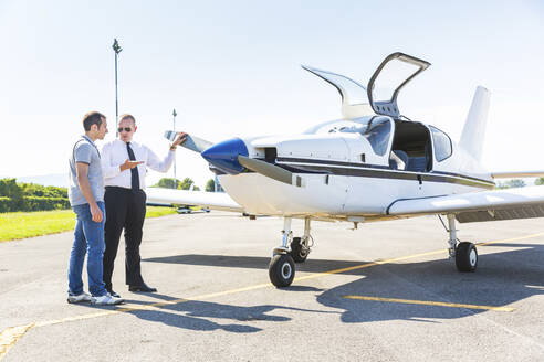 Pilot und Co-Pilot sitzen auf der Startbahn und unterhalten sich vor einem Sportflugzeug - WPEF02930