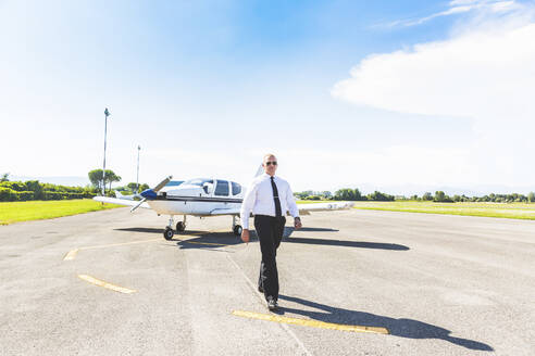 Pilot geht auf Startbahn, Sportflugzeug im Hintergrund - WPEF02932