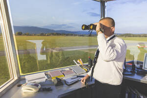 Pilot steht im Kontrollturm und benutzt ein Fernglas - WPEF02955