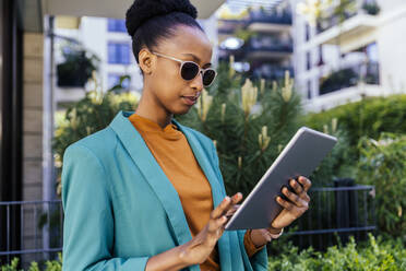 Porträt einer jungen Geschäftsfrau mit Sonnenbrille, die im Freien ein digitales Tablet benutzt - MFF05771