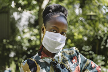 Portrait of young woman wearing white textile protective mask in garden - MFF05806