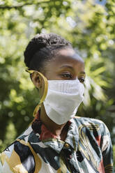 Portrait of young woman wearing white textile protective mask in garden - MFF05807