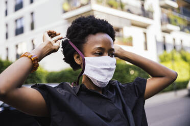 Portrait of young woman putting on protective mask outdoors - MFF05842