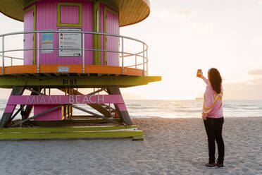 Frau fotografiert Rettungsschwimmer-Hütte am Strand von Miami bei Sonnenaufgang, Florida, USA - GEMF03789
