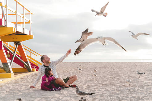 Vater füttert Möwen und sitzt mit seiner Tochter am Strand von Miami, Florida, USA - GEMF03796