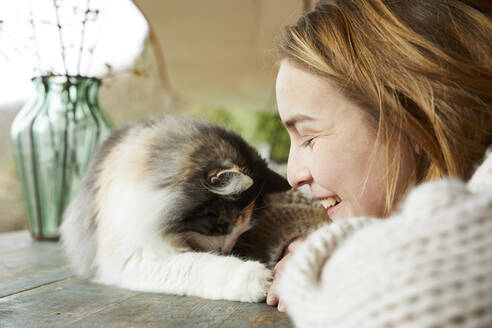 Glückliche Frau mit norwegischer Waldkatze auf Holztisch im Freien - FSF01092