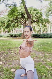 Mittlere erwachsene Frau übt Yoga auf einer Matte im Park - JNDF00157