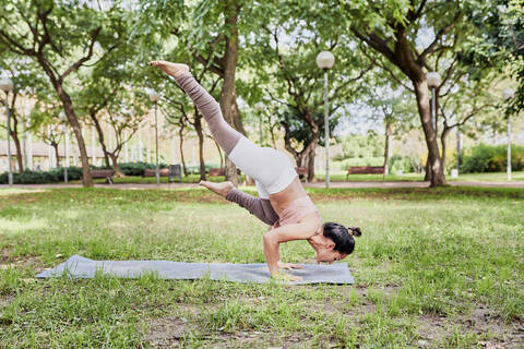 Mid adult woman practising yoga on mat in park, crow pose stock photo