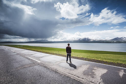 Georgia, Samtskhe-Javakheti, Poka, Young man standing at roadside admiring alpine lake - WVF01695