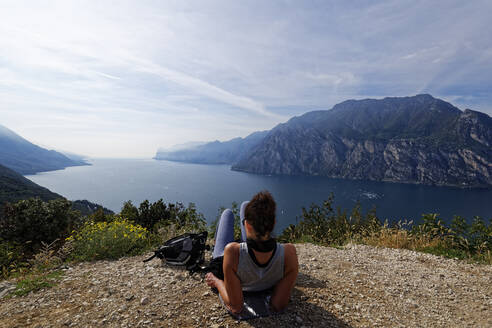 Italien, Trentino, Torbole, Rückansicht einer Frau mit Blick auf den von Bergen umgebenen Gardasee - UMF00937