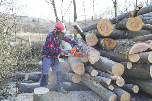 Lumberjack cutting log with chainsaw in forest - HMEF00942