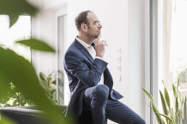 Nachdenklicher Geschäftsmann schaut aus dem Fenster - UUF20381