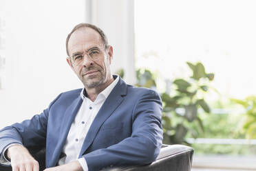 Portrait of mature businessman wearing glasses sitting in armchair - UUF20390