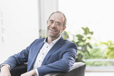 Portrait of relaxed businessman sitting in armchair - UUF20391