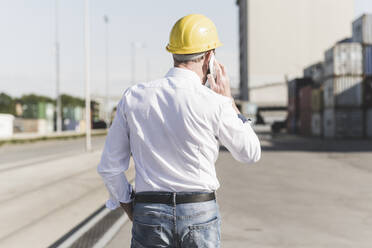 Rückansicht eines telefonierenden Geschäftsmannes mit Schutzhelm auf einem Industriegelände - UUF20404