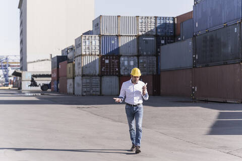 Geschäftsmann mit Schutzhelm bei der Nutzung eines Mobiltelefons auf einem Industriegelände, lizenzfreies Stockfoto