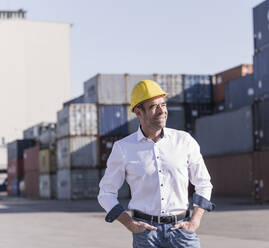 Porträt eines entspannten Geschäftsmannes mit Schutzhelm vor einem Frachtcontainer - UUF20412