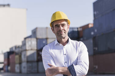 Porträt eines Geschäftsmannes mit Schutzhelm vor einem Frachtcontainer - UUF20413