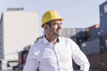 Porträt eines Geschäftsmannes mit Schutzhelm auf einem Industriegelände mit Blick in die Ferne - UUF20415