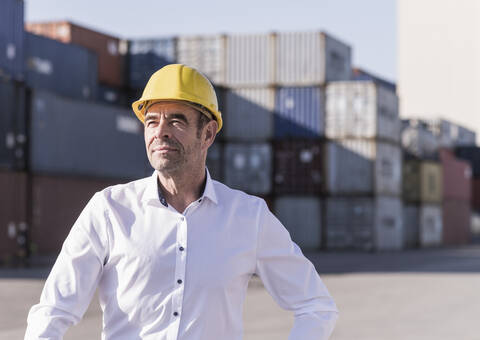 Porträt eines Geschäftsmannes mit Schutzhelm vor einem Frachtcontainer, lizenzfreies Stockfoto