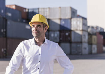Porträt eines Geschäftsmannes mit Schutzhelm vor einem Frachtcontainer - UUF20421