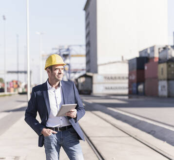 Businessman wearing safety helmet with digital tablet at industrial site - UUF20428