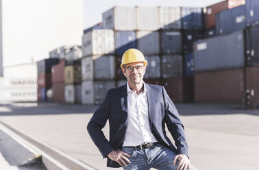 Porträt eines lächelnden Geschäftsmannes mit Schutzhelm auf einem Industriegelände - UUF20430
