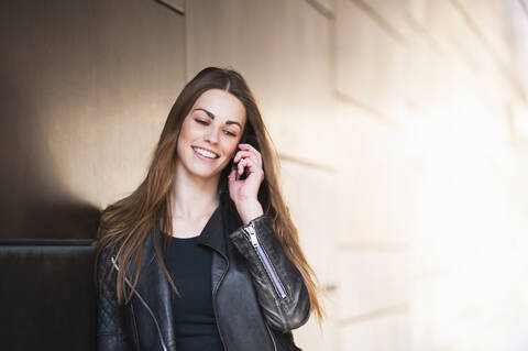 Happy young woman using smart phone by wall in city stock photo