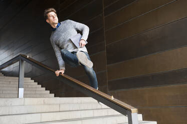 Young man jumping over railing at steps in underground walkway - DIGF12521