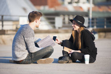 Glückliches Paar mit Smartphone und Laptop auf der Terrasse eines Gebäudes in der Stadt - DIGF12537