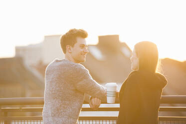 Glückliches Paar im Gespräch auf der Terrasse eines Gebäudes an einem sonnigen Tag - DIGF12542