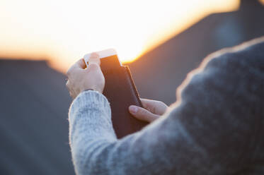 Ausgeschnittenes Bild einer Frau, die bei Sonnenuntergang ihr Smartphone aus der Hülle nimmt - DIGF12548