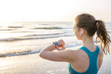 Sportliche Frau überprüft ihre Smartwatch am Meer - DIGF12567