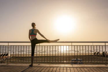 Sportliche Frau, die sich bei Sonnenaufgang an der Strandpromenade dehnt, Gran Canaria, Spanien - DIGF12573