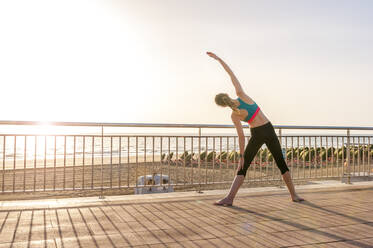 Sportliche Frau, die sich bei Sonnenaufgang an der Strandpromenade dehnt, Gran Canaria, Spanien - DIGF12574