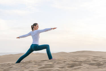 Woman practicing yoga at sunset in the dunes, Gran Canaria, Spain - DIGF12577