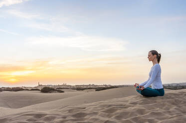 Woman practicing yoga at sunset in the dunes, Gran Canaria, Spain - DIGF12578