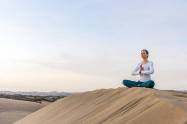 Woman practicing yoga at sunset in the dunes, Gran Canaria, Spain - DIGF12579