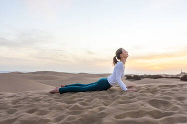 Woman practicing yoga at sunset in the dunes, Gran Canaria, Spain - DIGF12582