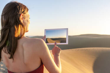 Frau beim Fotografieren mit Tablet bei Sonnenuntergang in den Dünen, Gran Canaria, Spanien - DIGF12601