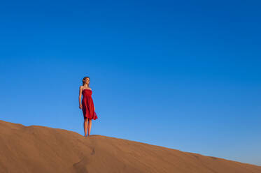 Frau in rotem Kleid steht in den Dünen unter blauem Himmel, Gran Canaria, Spanien - DIGF12604