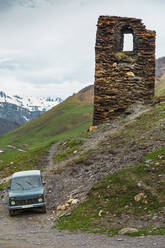 Georgien, Swanetien, Ushguli, Altes Auto vor altem mittelalterlichen Backsteinturm geparkt - WVF01747