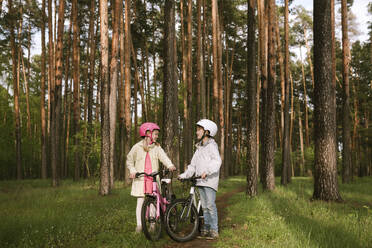 Mädchen und Junge stehen mit Fahrrädern im Wald - EYAF01080