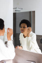 Mirror image of young woman applying mascara - GIOF08250