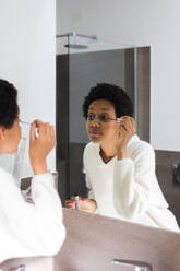 Spiegelbild einer jungen Frau, die Wimperntusche aufträgt - GIOF08250