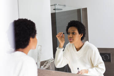 Mirror image of young woman applying mascara - GIOF08251